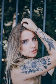 Close-up portrait of a woman with a floral tattoo on her arm, posing outdoors.